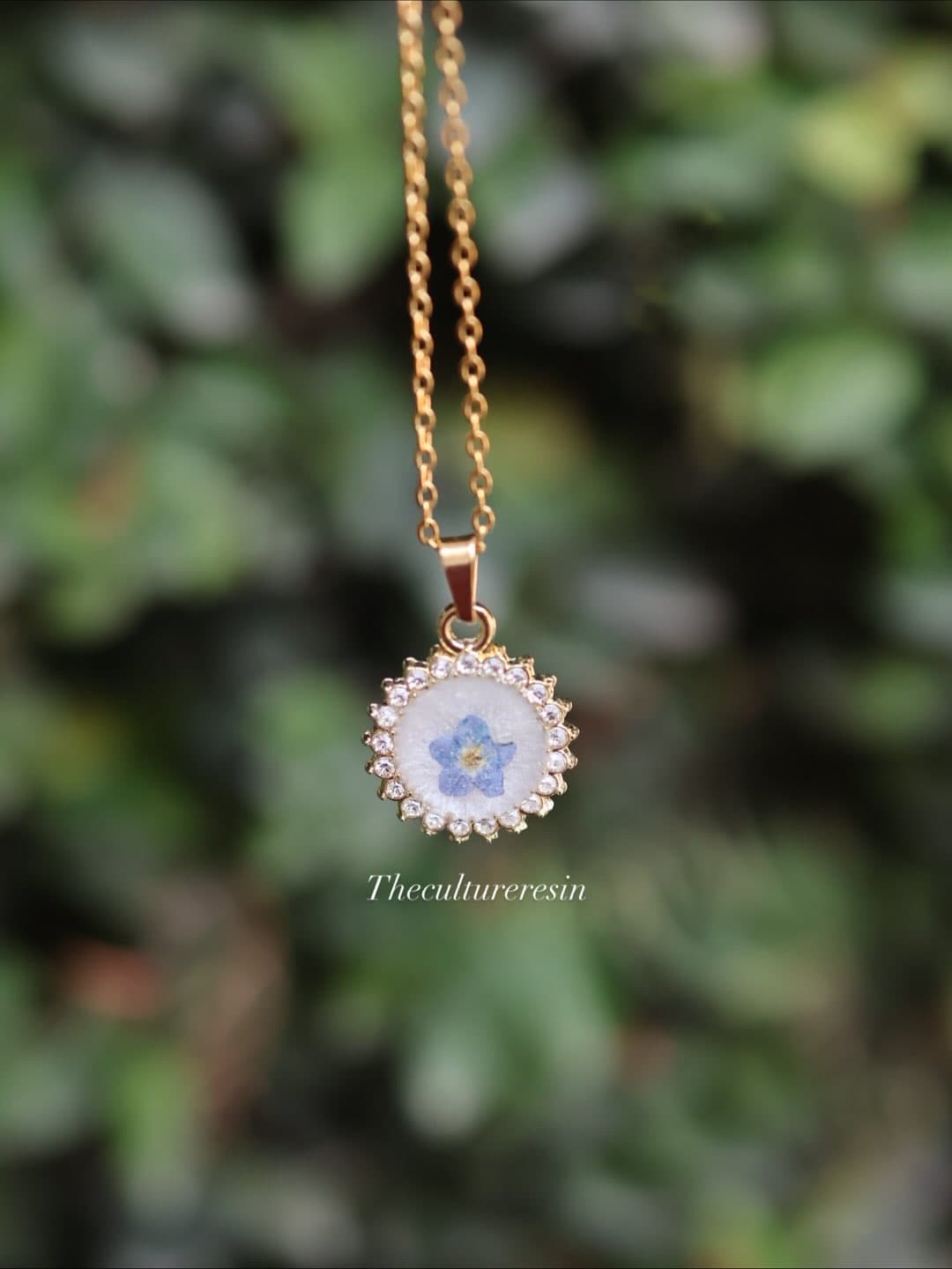 Round gold pendant holding a single pressed blue forget-me-not, on a fine gold chain